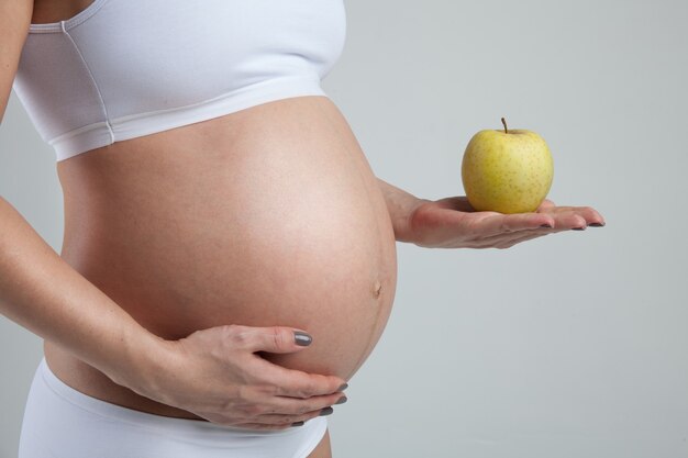 Bauch einer schwangeren Frau mit grünem Apfel auf ihrer Hand lokalisiert auf weißem Hintergrund