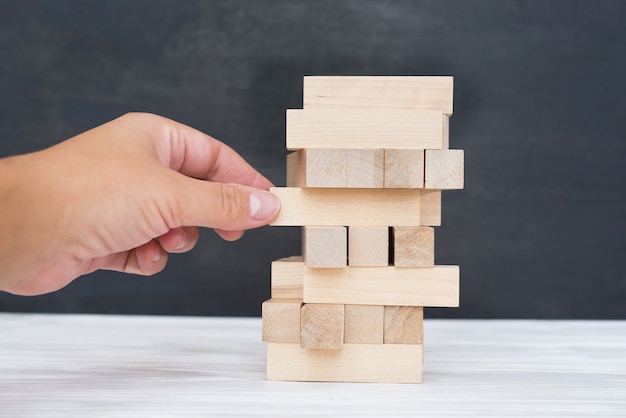 Bauen aus Holzblöcken. Holzklötze stapeln Spiel mit der Hand im Hintergrund. Konzeptionelle der Teamarbeit. Blockturm mit Architekturmodell, Risiko-Management- und Strategieplan, Wachstumsgeschäftserfolg