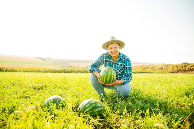 Bauer hält eine Wassermelone in der Hand schaut in die Kamera, der Mann ist glücklicher kaukasischer Mann mit Hut o...