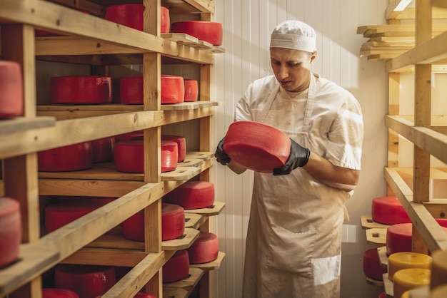 Bauer in Handschuhen dreht Käseköpfe im Käsereifelager um Produktion von Käse und Milchprodukten