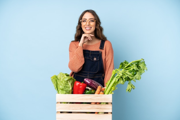 Bauer mit frisch gepflücktem Gemüse in einer Schachtel mit Gläsern und lächelnd