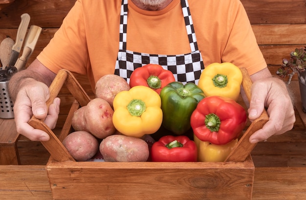 Bauernhände halten rohes gemüse über einem holzkorb, kartoffeln und paprika, ernährung und gesunder lebensstil - aktives konzept für ältere menschen im ruhestand