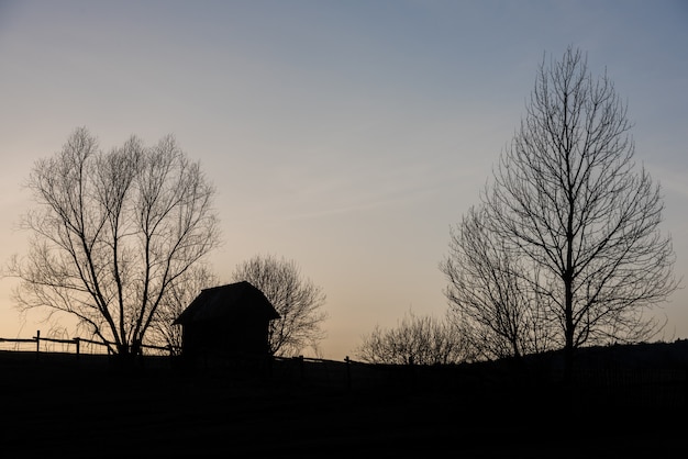 Bauernhof in Ost-Europa mit Zaun und Bäumen im Sonnenunterganghintergrund.