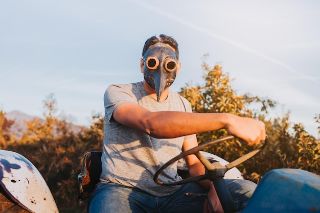 Bauernmann mit der Pestmaske beim Fahren eines alten Traktors mitten auf seinem Ackerland