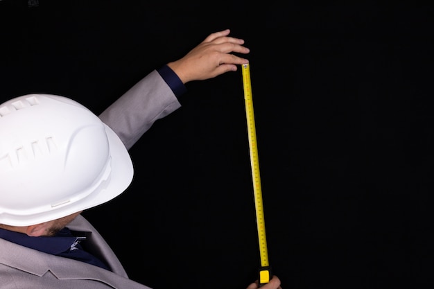 Bauingenieur Geschäftsmann in einem weißen Helm misst die Entfernung mit einem Maßband