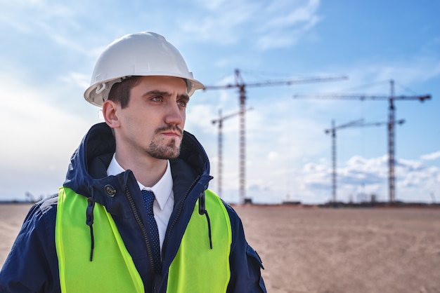 Bauingenieur in einem weißen Helm und einer blauen Jacke auf der Baustelle