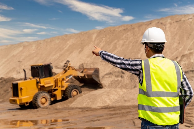 Bauingenieur kontrolliert die arbeit des gelben baggers, der auf der baustelle der sandgruben-sandindustrie arbeitet