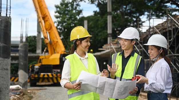 Bauingenieurteam in gelben Westen bespricht gemeinsam den Bauablauf auf der offenen Baustelle in der Nähe des Krans