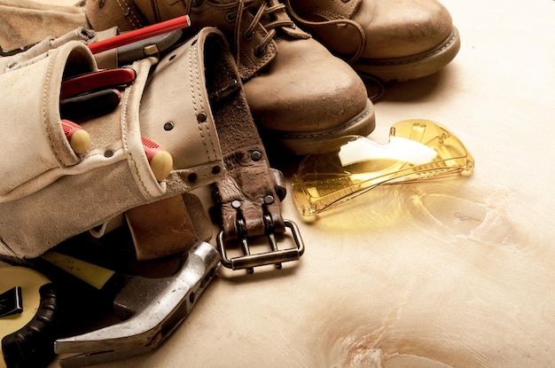 Foto baukonzepthintergrund von werkzeuggürtel, gelben stiefeln, schutzbrillen und ameisenwerkzeugen auf sperrholz