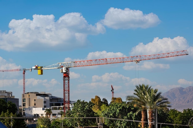 Foto baukranen über dem unfertigen wohngebäude gegen einen wolkenhimmel große baustelle mit zwei kranen, die an einem gebäudekomplex mit palmen in der stadtlandschaft arbeiten