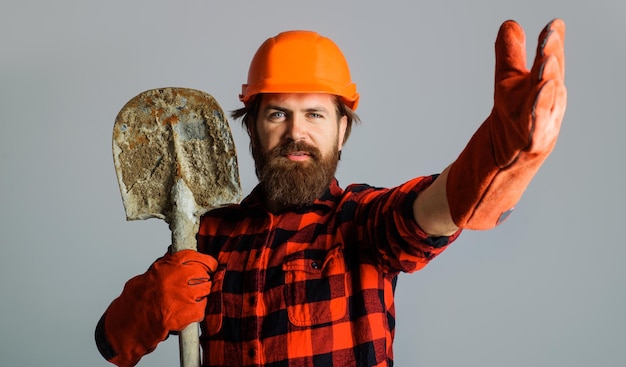 Baumeister mit Schutzhelm und Arbeitshandschuhen mit Schaufel bärtiger Arbeiter mit Schutzhelm mit Spaten