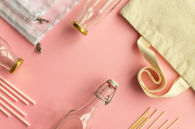 Baumwoll-Einkaufstaschen aus Stoff, Glasflaschen, Papierstrohhalme und Holzstäbchen auf rosafarbenem Hintergrund. Ansicht von oben. Platz kopieren.