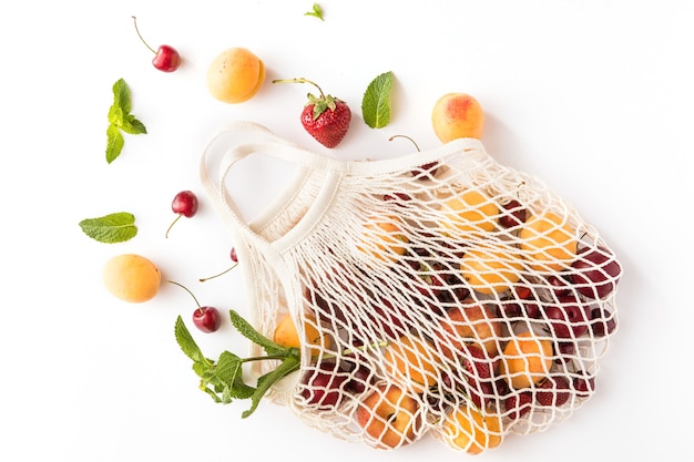 Baumwoll-Öko-Netzbeutel mit saisonalen Bio-Früchten auf weißem Hintergrund. Umweltfreundliches Konzept