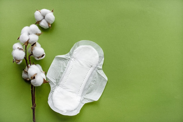 Baumwollblume auf grünem Papierhintergrund und Damenbinden für Frauen Draufsicht Das Konzept der Hygiene und der Gesundheit von Frauen