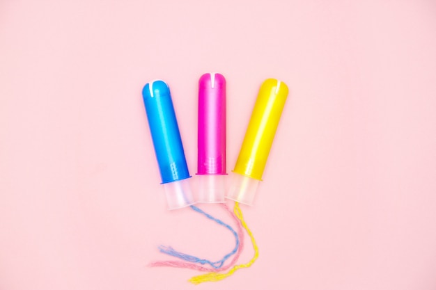 Baumwolltampons des menstruationszyklus drei mit blauen rosa gelben applikatoren auf rosa