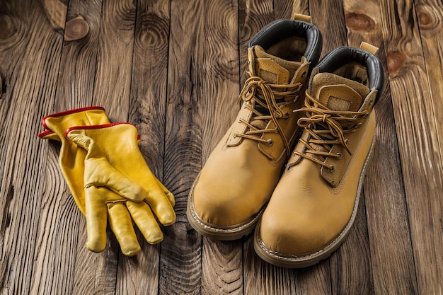 Bausicherheitswerkzeuge gelbe Arbeitshandschuhe und Arbeitsstiefel aus Leder auf Vintage-Holzhintergrund