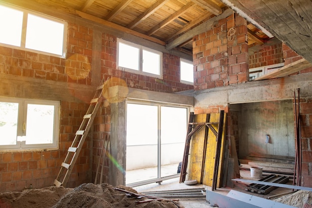 Foto baustelleninnenraum einer neuen zweistöckigen wohnung mit fenstern und roten backsteinwänden. baustelle zum neuen haus im gange