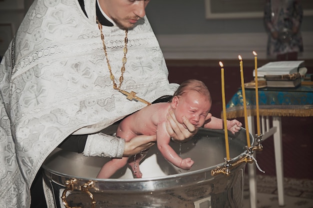 Foto bautismo infantil en la iglesia ortodoxa. el sacerdote sostiene al niño recién nacido en sus brazos en la pila bautismal con agua bendita. el bebé se baña en agua. rito sacramental del bautismo