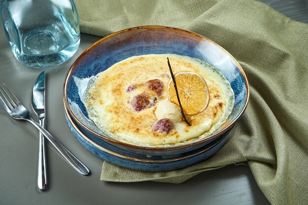 Baya gratinada con helado en un recipiente azul sobre la mesa de madera. Postre horneado francés sabroso y dulce