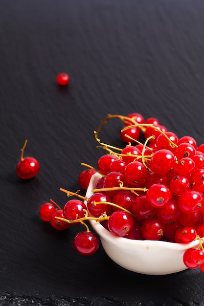 Baya de grosella roja de fruta de verano en taza de cerámica en el tablero de piedra pizarra negra con espacio de copia