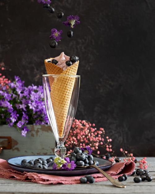 Bayas de arándanos en una taza de waffle rodeada de flores púrpuras y bayas. Tema de verano Levitación