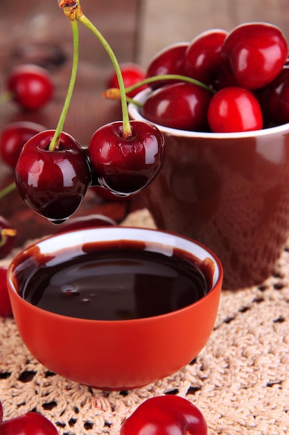 Bayas de cereza rojas maduras en taza y salsa de chocolate en primer plano de la mesa de madera