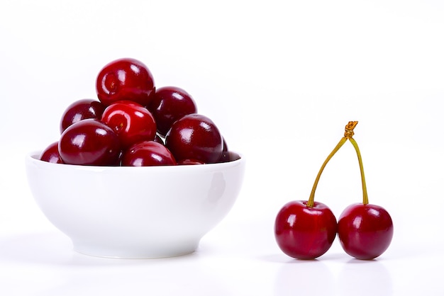 Bayas de cereza en una taza blanca sobre un fondo blanco. Aislado. Cerezas maduras. Cereza roja deliciosa. Lugar para publicidad, rotulación, logotipo, texto, diseño, maqueta.