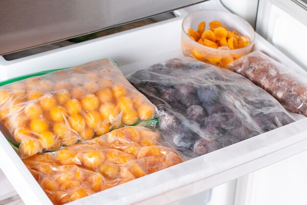 Foto bayas congeladas en el congelador. ciruelas congeladas, ciruelas cereza en el estante del congelador.
