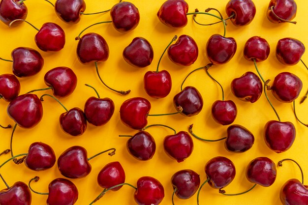 Foto bayas dispersas de cerezas maduras sobre un fondo amarillo brillante. vista superior. vitaminas estacionales.