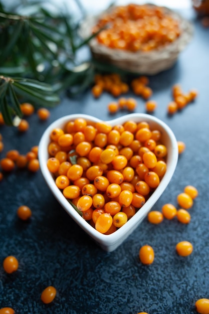 Bayas de espino marino en un cuenco en forma de corazón naranja bayas saludables macro estilo rústico vista desde arriba