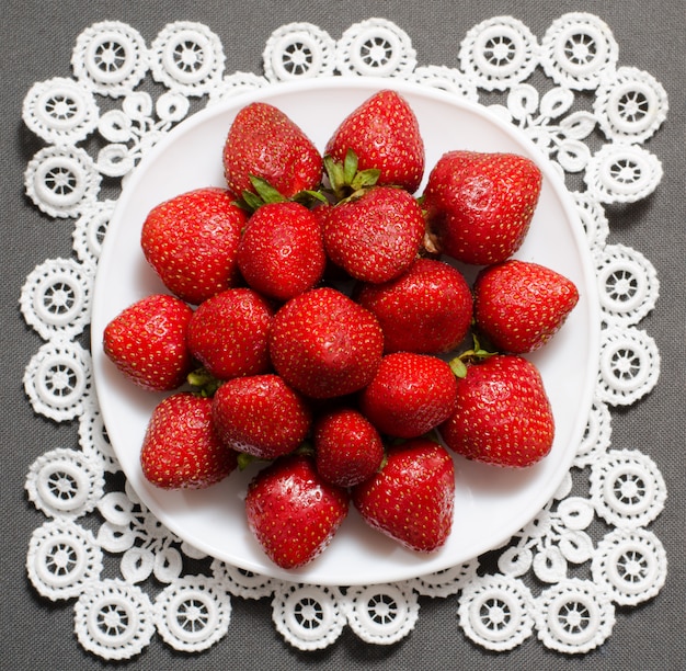 Bayas fresas maduras en el plato en servilleta de encaje, vista superior, gris