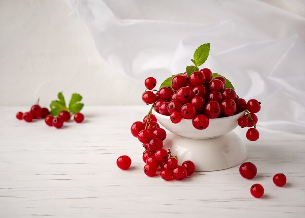 Bayas frescas de grosella roja se encuentran en una taza sobre un fondo blanco.