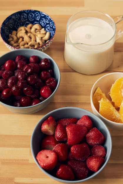 Bayas frescas naranja nueces en tazones y leche en jarra