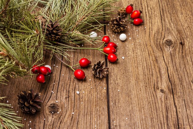 Bayas frescas de rosa de perro, caramelos de bolas, ramas y conos de pino, nieve artificial. Decoraciones de la naturaleza, tableros de madera vintage