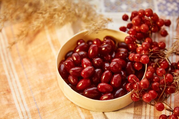 Bayas orgánicas de otoño de viburnum y cornejo en un tazón de madera en el acogedor interior de una casa Comida saludable para compota de té y concepto de mermelada Vista superior espacio de copia de fondo Foto de alta calidad