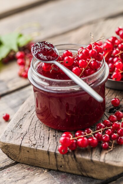 Bayas rojas, jugosas de grosellas rojas y frascos de mermelada de bayas en una mesa de madera