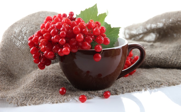 Bayas rojas y naranjas en taza, sobre una servilleta de tela de saco, aislado en blanco