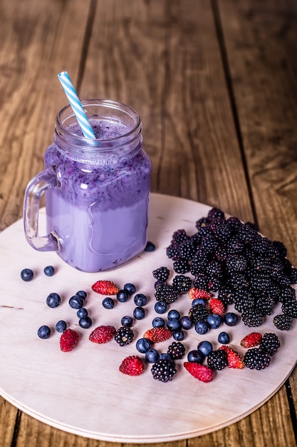 Bayas salvajes del smoothie hecho en casa fresco del yogur en un tarro de cristal en un viejo vintage, primer, visión superior, foco selectivo. Cosecha