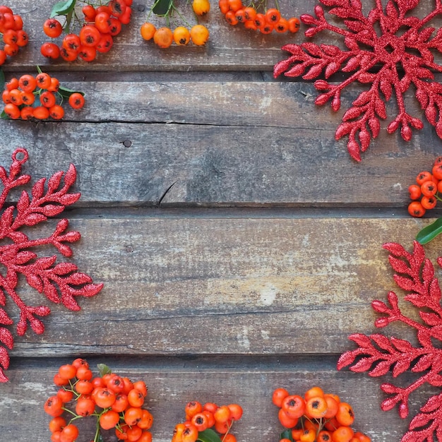 Bayas de serbal de invierno rojas, naranjas y amarillas sobre un fondo de madera horizontal Los copos de nieve grandes y brillantes rojos están dispuestos en un círculo alrededor del fondo de los bordes Telón de fondo natural de Año Nuevo o Navidad