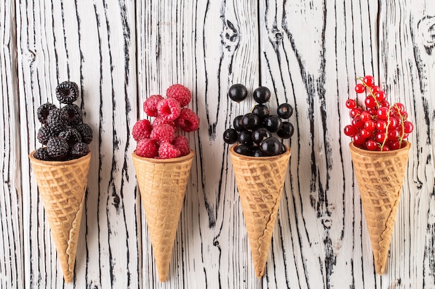 Bayas de verano en cono de waffle sobre fondo blanco de madera