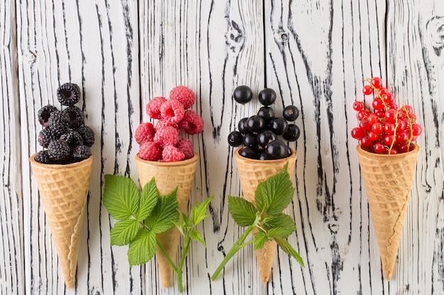 Bayas de verano en cono de waffle sobre fondo blanco de madera