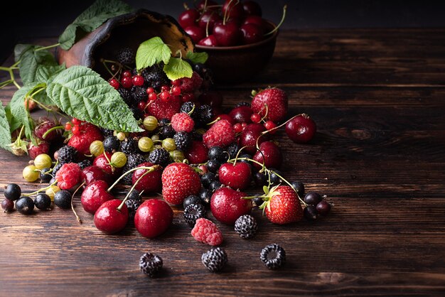 Bayas de verano, frambuesas, fresas, cerezas, grosellas esparcidas sobre una mesa de madera oscura, comida sana, primer plano.