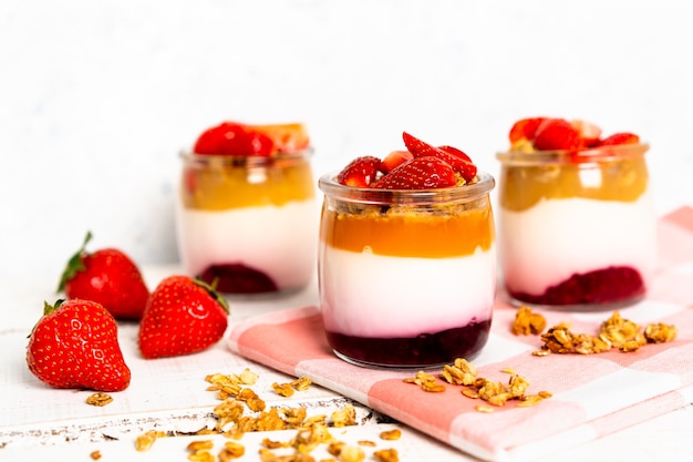 Bayas de yogur de frutas con muesli y fresas frescas, sobre un fondo de madera blanca, saludable