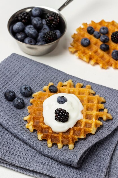 Bayas y yogur en gofres en una servilleta gris Moras y arándanos en un recipiente de metal en la mesa