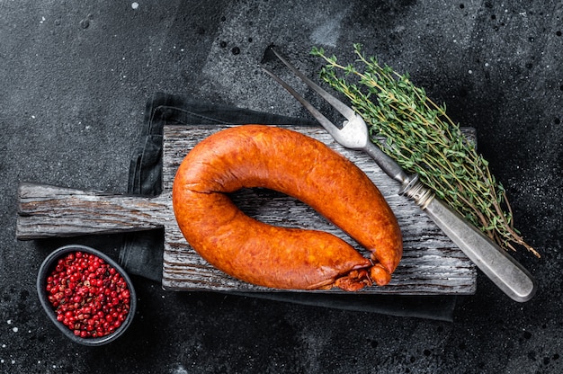 Bayerische geräucherte Wurst auf einem rustikalen Holzbrett mit Thymian. Schwarzer Hintergrund. Ansicht von oben.