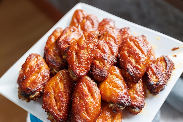 Foto bbq chicken wings auf einem weißen quadratischen teller.