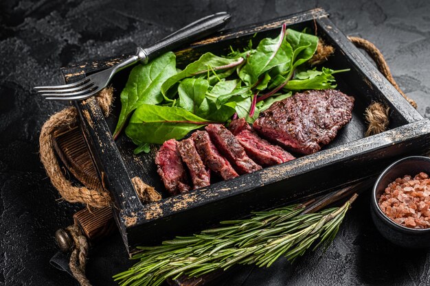 BBQ gebratenes Flankensteak im Holztablett mit Gemüsesalat Schwarzer Hintergrund Draufsicht