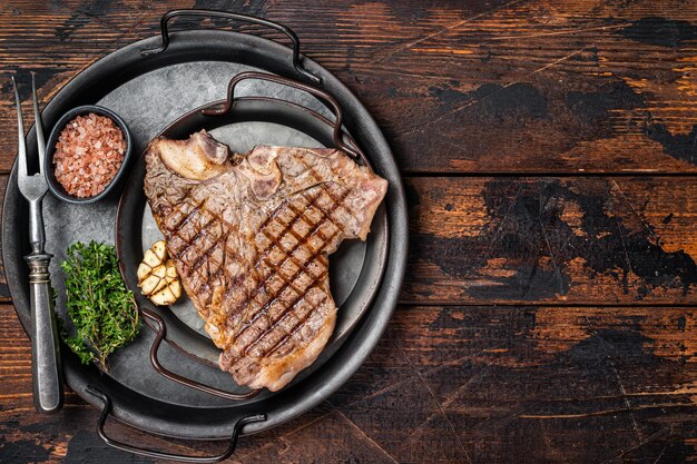 Foto bbq grilled tbone ou porterhouse carne de vaca bife em uma bandeja de aço com ervas fundo de madeira vista superior espaço de cópia