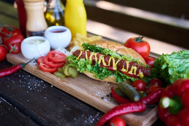 Bbq-Hotdog, serviert mit Gemüse und Pommes Frites und Saucen auf Holzbrett