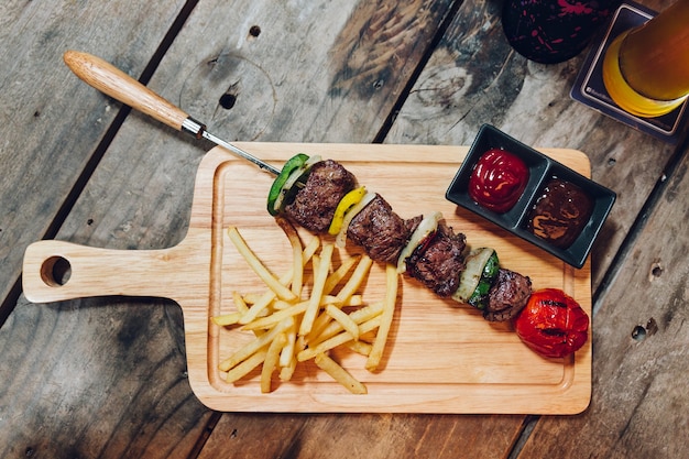 BBQ-Rindfleisch-Kebab diente mit Pommes-Frites, Tomatensauce und BBQ-Soße auf hölzerner Platte.